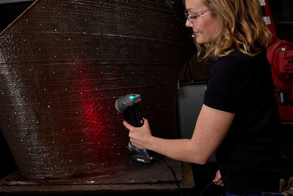 An engineer uses a 3D scanner to inspect a large 3D-printed stainless steel part