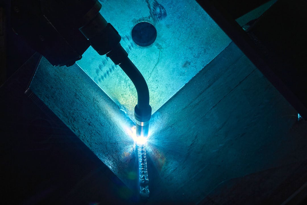 A close-up shot of a Lincoln Electric robotic MIG/GMAW welding system welding steel