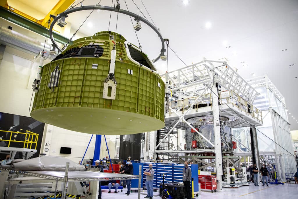 An aerospace pressure vessel is lifted by overhead crane onto a work stand.